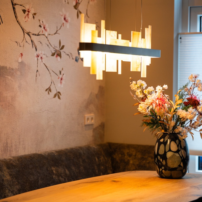 Dining room detail with wooden table, vase of flowers, designer pendant lamp and blossom-print wallpaper in the modernly renovated home in the Geuzenkwartier