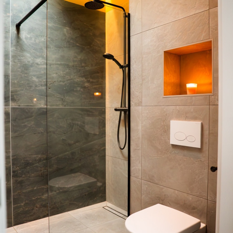 Modern bathroom with walk-in shower, glass screen, wall-hung toilet and illuminated wall niche, part of the sustainable home renovation in the Geuzenkwartier, The Hague