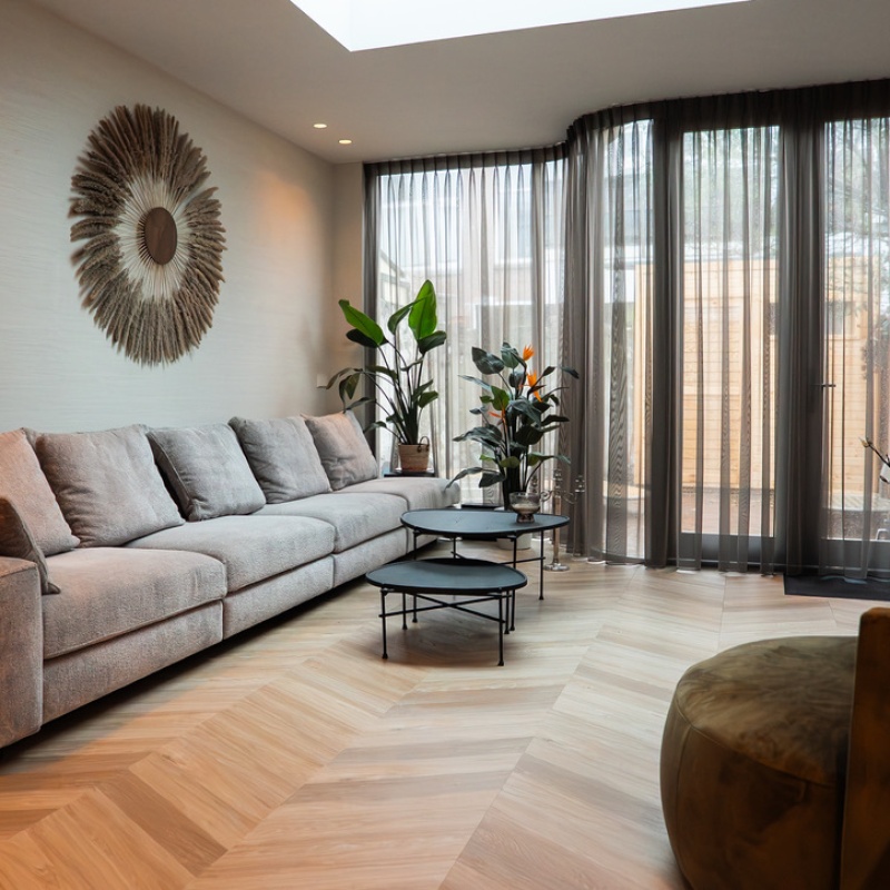 Spacious, bright living room with large grey corner sofa, herringbone floor and floor-to-ceiling windows in the extended and sustainably renovated home in The Hague