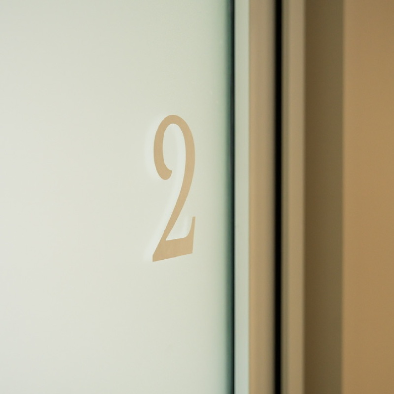Glass door of treatment room 2 with a gold-coloured room number