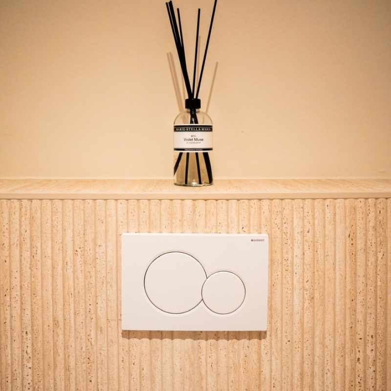 Detail of the restroom with a reed diffuser and flush plate on a travertine wall