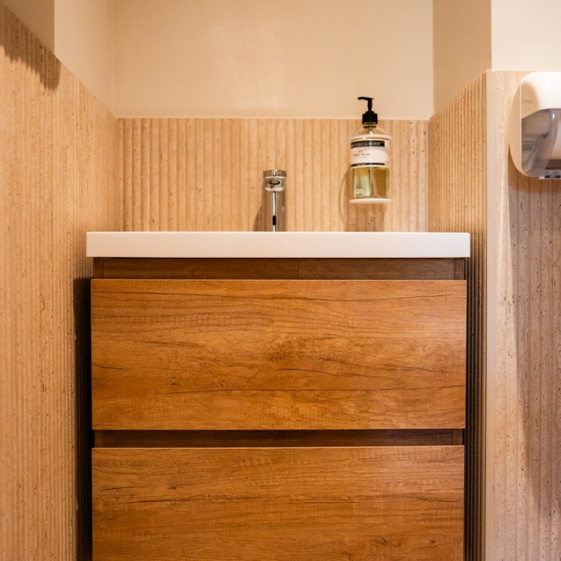 Restroom with a wooden vanity unit and travertine wall cladding
